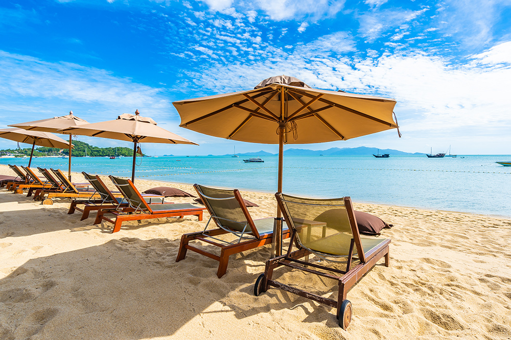Beautiful tropical beach sea and ocean with coconut palm tree  and umbrella and chair on blue sky and white cloud for holiday vacation travel